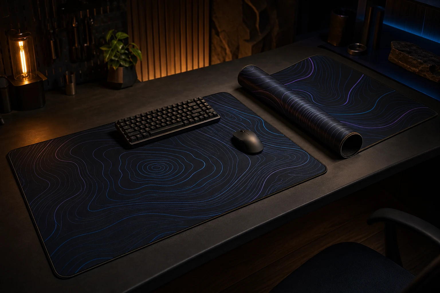 Two dark stitched desk mats with subtle cyan and violet contour patterns on a lit workbench.